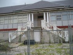 an old building behind a fence with a dog crate in the foreground and stairs leading up to it