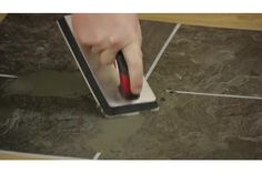 a person is using a mop to clean the tile on the floor with a red and black handle