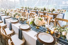 a table set up with white and blue flowers, gold rimmed plates and place settings