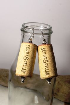 two cork earrings with words on them are hanging from a glass jar filled with water