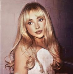 a woman with long blonde hair and blue eyes posing for a photo in front of a brick wall