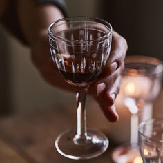 a person holding a wine glass in front of two glasses on a table with candles