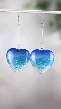 two heart shaped glass earrings hanging from a hook on a white string with blue and green glitter