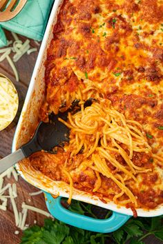 a blue casserole dish filled with spaghetti and meat sauce on a wooden table