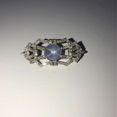 A Ladies Platinum 1 3/4 Inch Long Antique Brooch Set With A 12 Mm Round Natural Blue Grey Star Sapphire Weighing Approximately 10 Carats. The Brooch Is Also Set With 104 Round Diamonds And 6 Marquise Cut Diamonds Having A Combined Weight Of Approximately 1.33 Carats. Vintage Blue Diamond Brooch, Vintage Blue Diamond Brooches, Elegant Star-shaped Wedding Brooch, Elegant Star-shaped Brooch Jewelry, Elegant Star-shaped Brooch, Elegant Star-shaped Jewelry Brooch, Formal Star-shaped Brooch Jewelry, Vintage Star-shaped Brooches For Formal Occasions, Vintage Star Brooches For Formal Occasion