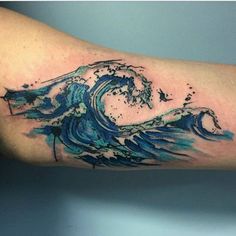 a blue wave tattoo on the arm with water splashing down it's side