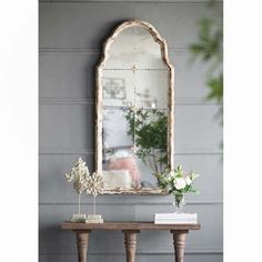 a table with a mirror and flowers on it in front of a gray painted wall