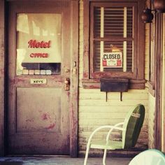 a green chair sitting in front of a closed sign on the door to a motel