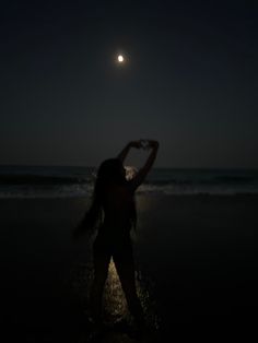 a woman standing on the beach at night with her arms in the air, looking into the distance