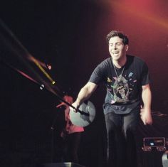 a young man holding a pair of drums in front of a stage with other people