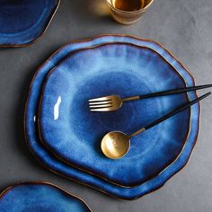 blue plates with gold rims and forks on them, next to two empty cups