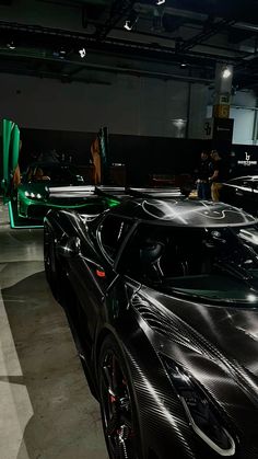 a black sports car parked in a garage with people looking at the cars behind it