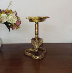 a brass cobra on a table next to a vase with flowers