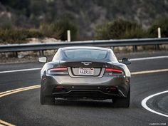 the back end of a silver sports car driving down a road