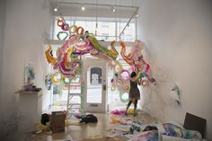 a woman is standing on a ladder in front of a room with many pieces of art hanging from the ceiling