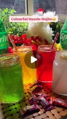 four different colored drinks sitting on top of a table next to flowers and bottles with straws in them