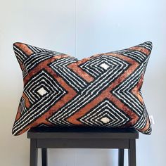 an orange and black pillow sitting on top of a wooden stool