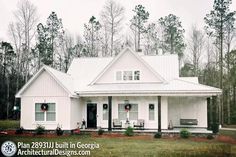 a white house in the middle of a field with trees around it and wreaths on the front door