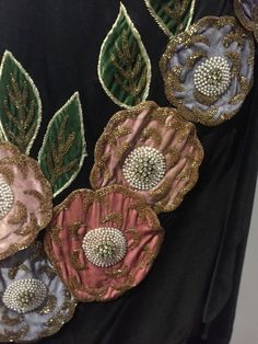 four different colored flowers with green leaves on black fabric and gold sequins in the center