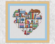 a cross stitch heart with books and a cat on it's shelf in the shape of a bookcase