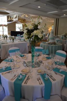 a table set up for a wedding with blue and white linens, silverware and flowers