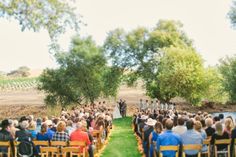 an outdoor wedding ceremony with people sitting in chairs and facing each other on the grass