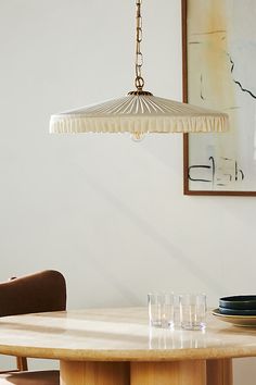 a wooden table topped with glasses under a hanging light over the dining room table and chairs