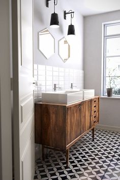 a bathroom with black and white tile flooring and two sinks on the vanity next to each other