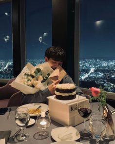 a young man sitting at a table with a cake and flowers in front of him