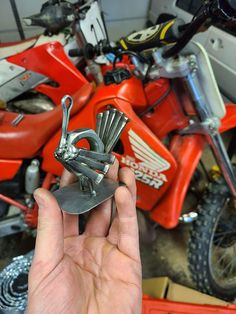 a hand holding a metal object in front of a red motorcycle