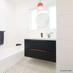 a bathroom with black and white flooring and a round mirror above the bathtub