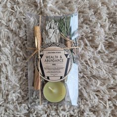 a packaged candle and some cinnamon sticks on a carpeted area with a tag that says, health & abundance