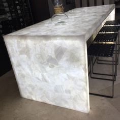 a white marble counter top sitting next to a wine glass on a metal rack in a kitchen