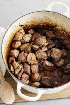 a pot filled with meat sitting on top of a cutting board next to a wooden spoon