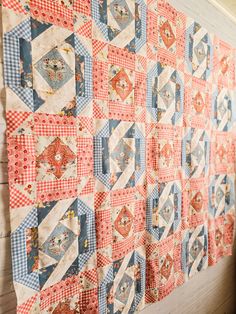 an old quilt hanging on the wall next to a wooden table with a red and white checkered cloth