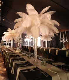 the table is set with place settings and tall centerpieces that are adorned with white feathers