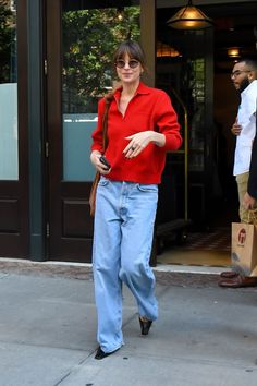 a woman in red shirt and jeans walking down the street