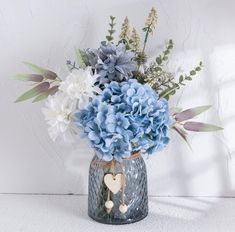 a vase filled with blue and white flowers on top of a table next to a wall