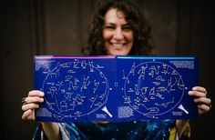 a woman holding up a blue book with stars and planets written on it in front of her face