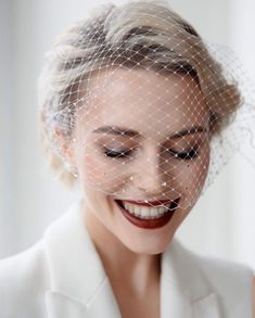 a woman wearing a veil and smiling at the camera with her eyes closed while she wears a white suit