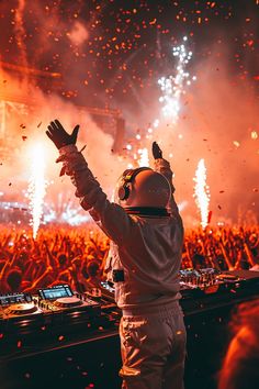 a dj in front of a large crowd at a music festival with his hands up