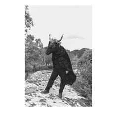 a black and white photo of a man with horns on his head walking up a hill