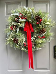 a christmas wreath on the front door with red ribbon and pine cones hanging from it