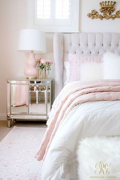 a white bed with pink and gold decor in a bedroom next to a mirrored nightstand