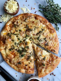 a pizza sitting on top of a white plate next to a bowl of cheese and herbs