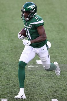 a football player running with the ball in his hand and wearing a green uniform on