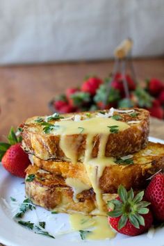 two pieces of french toast with cheese and strawberries on a white plate next to a basket of strawberries