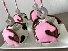 three decorated cupcakes on a plate with pink and white frosting, one is shaped like a cow