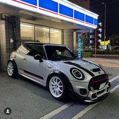 a silver and black mini cooper parked in front of a gas station at night time