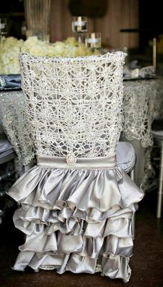 the back of a chair with ruffles and lace on it in front of a table